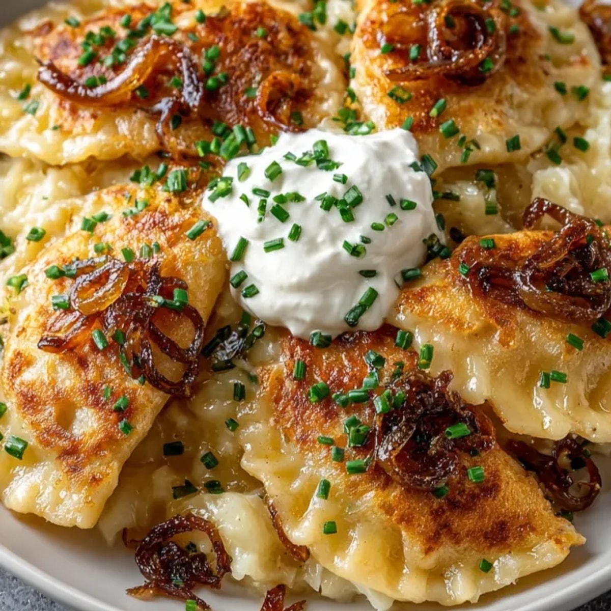 Kremowe pierogi ziemniaczano-serowe, gotowe do podania, polane cebulką i kleksem śmietany.