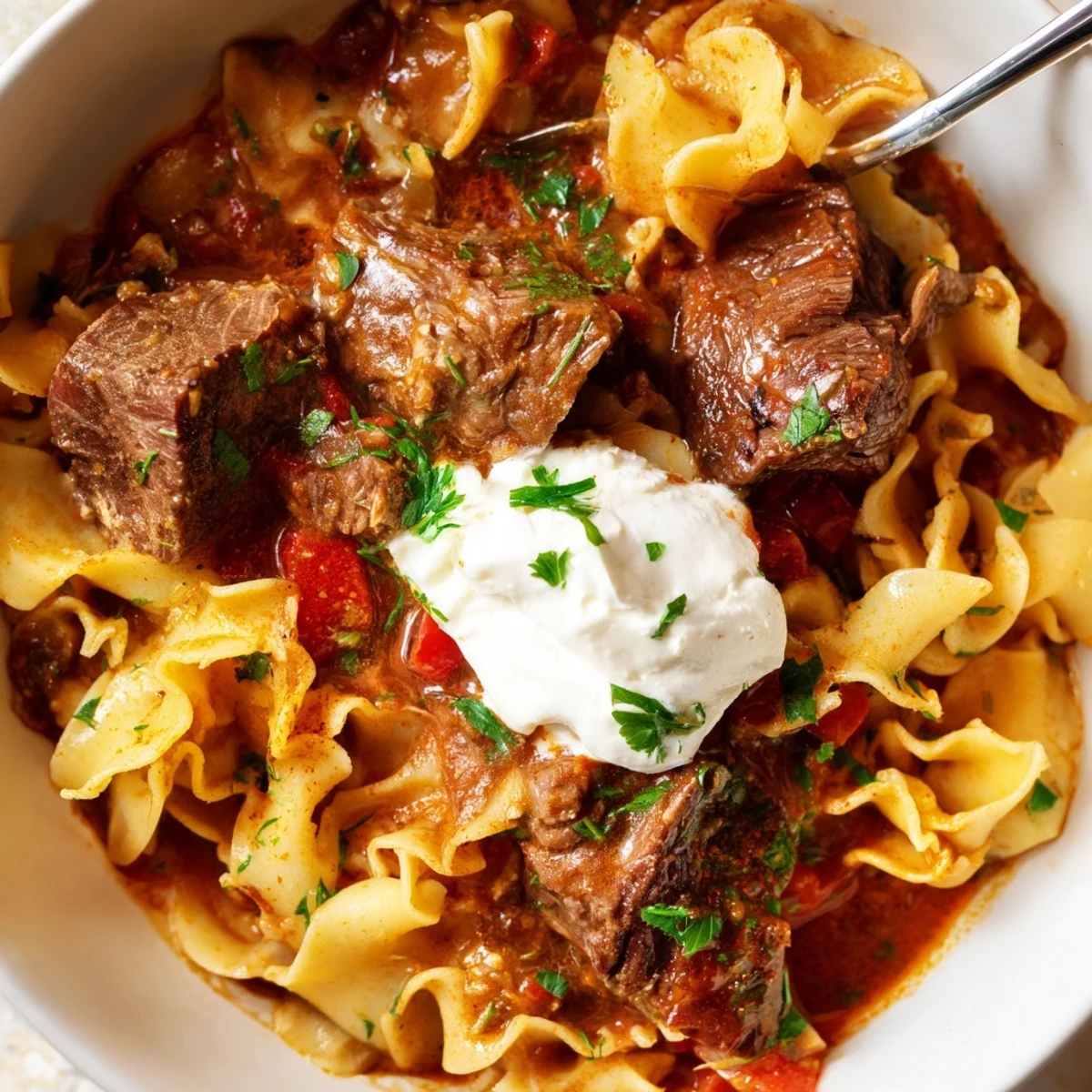 Gulasz z duszoną wołowiną podany na wspaniale przypieczonych makaronach.