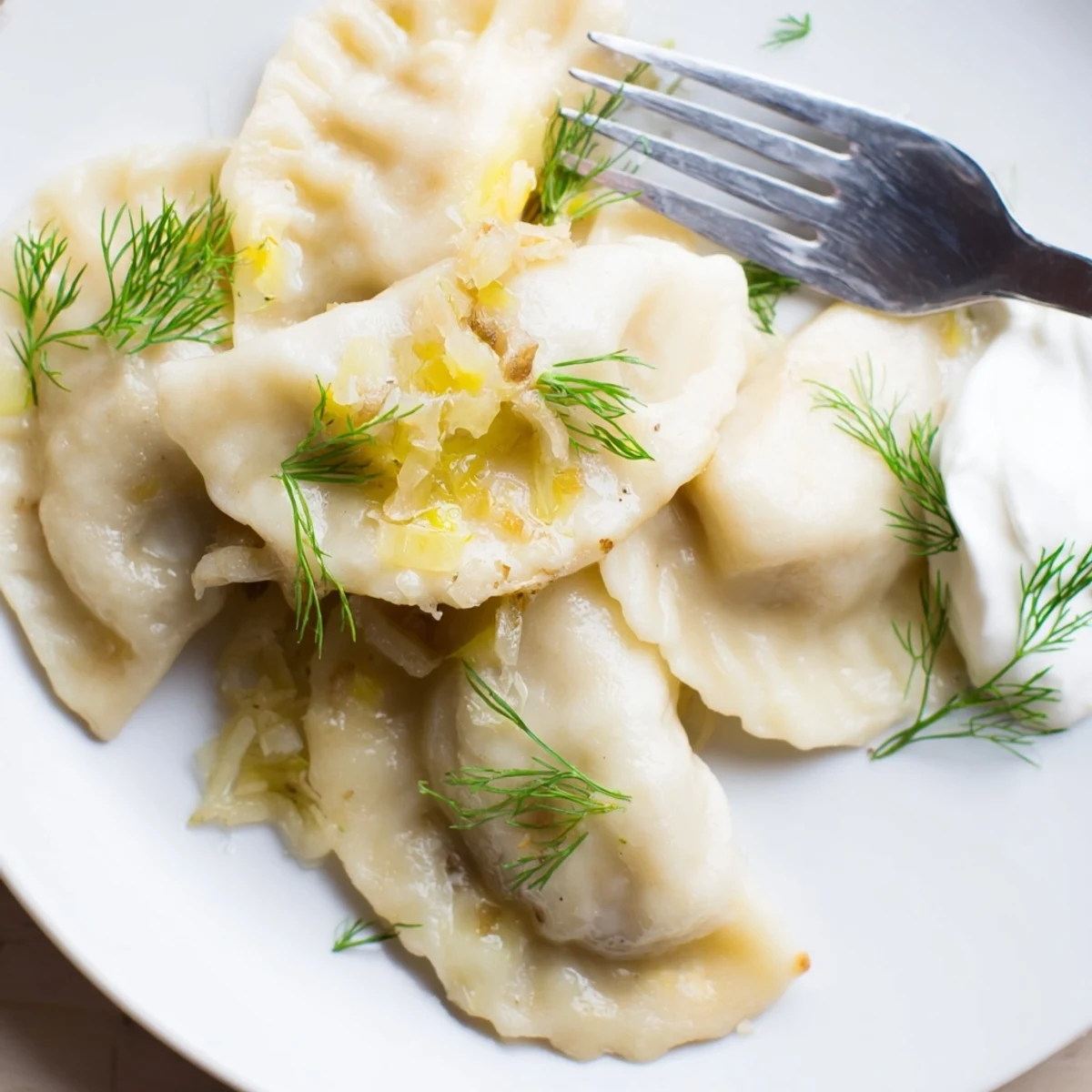 Delikatne pierogi z kapustą i grzybami, podane z kremowym sosem na wierzchu.  