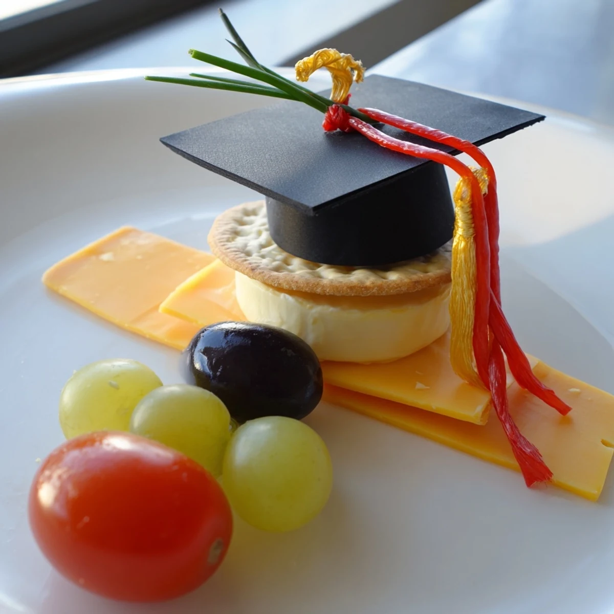 Apetyczny talerz w kształcie czapki absolwenta, pełen sera, warzyw i pysznych smakołyków.