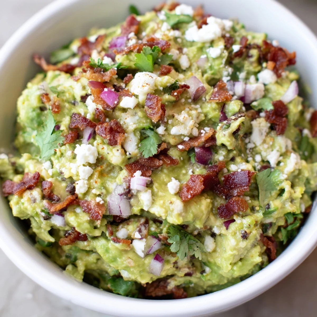 Creamy avocado mash dotted with crispy bacon bits and crumbled Cotija cheese, ideal for dipping.