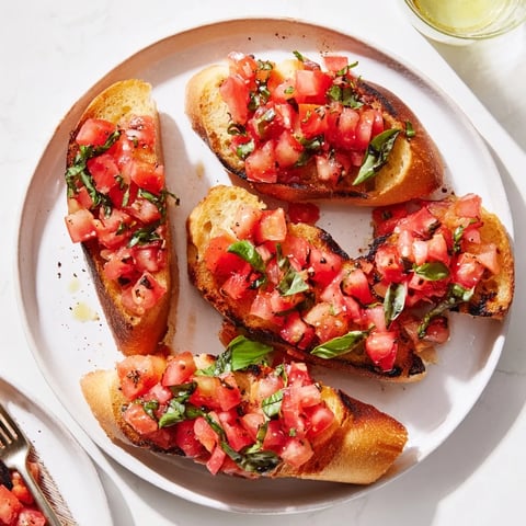 Chrupiące tosty bruschetta podane w eleganckiej linii, udekorowane świeżymi liśćmi bazylii i sosem.
