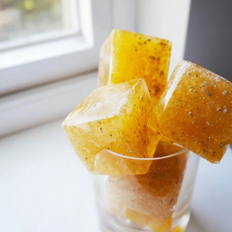Frozen Lemon Ginger Turmeric Wellness Cubes in a clear ice cube tray, glistening with natural zest and golden hue.