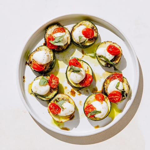 Close-up of vibrant Zucchini Caprese Bites, a simple Italian appetizer with fresh basil garnish.
