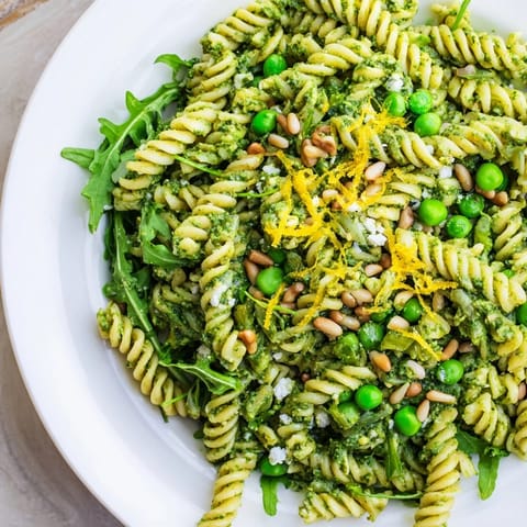 Apetyczna sałatka z zielonym pesto z makaronu, obficie posypana prażonymi orzeszkami pini.