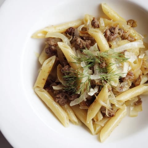 Makaron z kiełbasą i koprem włoskim na patelni, gotowy do podania z parmezanem i ziołami.