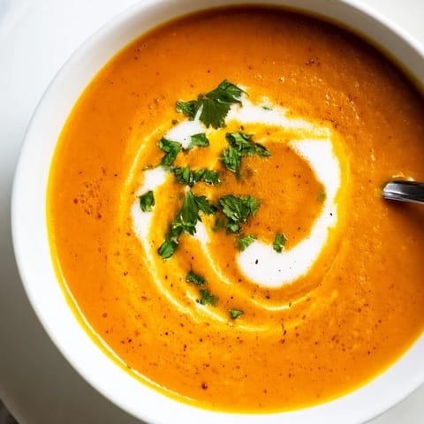 Dymna zupa marchewkowa z soczewicą, z domowym pieczywem i kwaśną śmietaną na stole w słonecznej kuchni.  