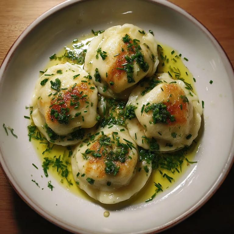 Na tle ciemnego tła, na białym talercie, siedzą trzy Tatra Cheese Dumplings z Chive Oil.