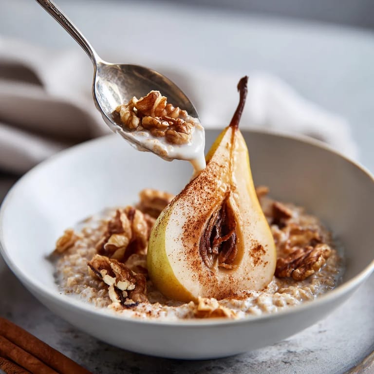 W white bowl, there is a piece of fruit with a spoon in it. The fruit is a pear, and the spoon is filled with cinnamon.