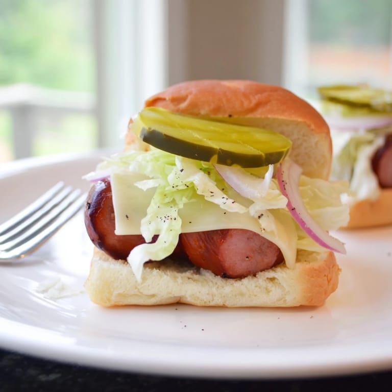 Kielbasa w mini burgerach z delikatnym serem i piklowanymi ogórkami, idealne na przyjęcie.