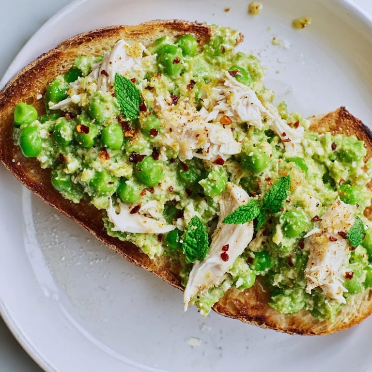 A close-up of vibrant smashed pea & chicken toast, showing the texture of the peas and shredded chicken.