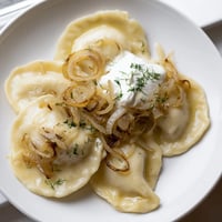 Golden fried Authentic Potato and Cheese Pierogi Ruskie, served hot with sour cream and fried onions.