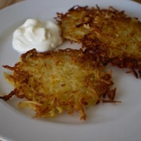 Złociste, chrupiące polskie placki ziemniaczane, podane na talerzu z kremową śmietaną i jabłkami.