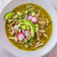 A vibrant bowl of Chicken Chili Verde with tender shredded chicken in a bright green tomatillo sauce, topped with fresh cilantro and avocado.