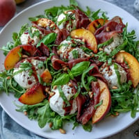 Letni plaster brzoskwiniowy z kremową burratą i solonym prosciutto w salacie.